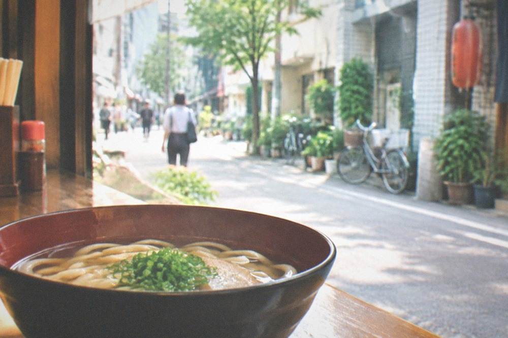 Soft udon noodles in clear dashi broth in a lacquer bowl on a shop counter
