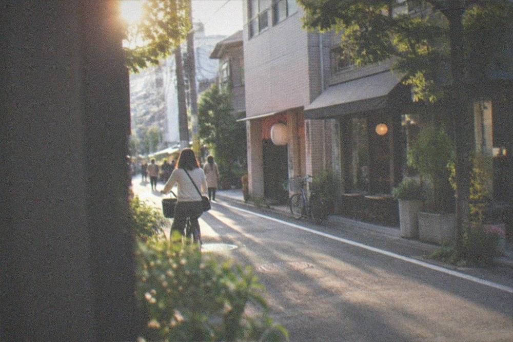 A cyclist on a quiet city street passing small shopfronts and cafe fronts