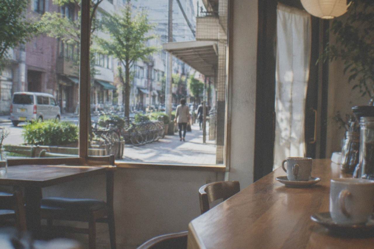 A quiet cafe interior with wooden tables, cups of coffee on a counter, and a window onto a city street