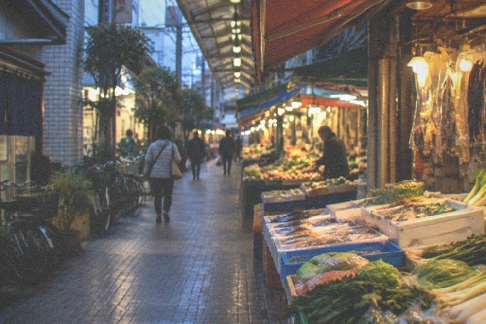 A covered food market aisle with stalls of vegetables, fish and dry goods under warm lighting