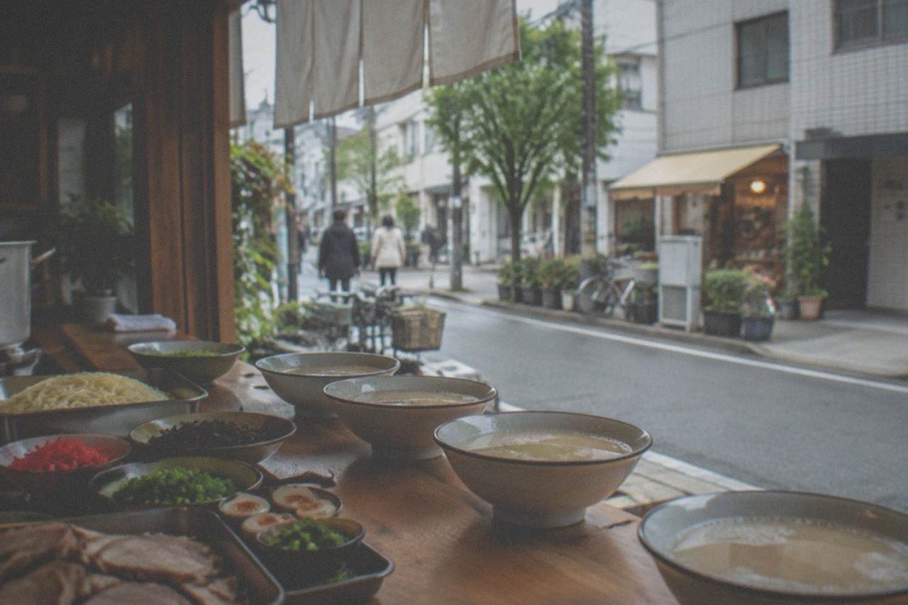 A small teaching kitchen with a wooden counter, bowls of pork broth, noodles and toppings set out ready for a class