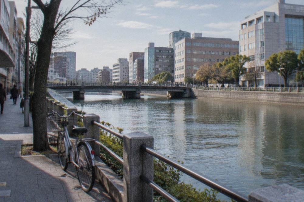 A bicycle parked on a quiet street beside a canal in central Fukuoka with the city skyline behind it