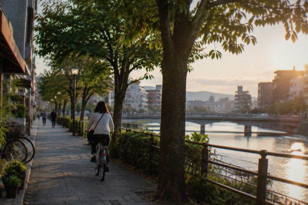 A cyclist riding along a tree-lined path beside the Naka River in Fukuoka