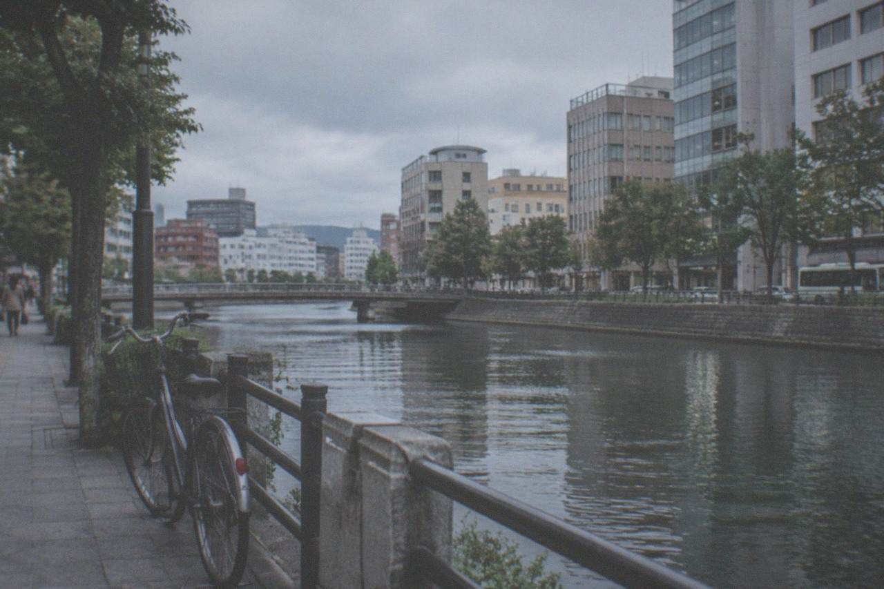 A bicycle parked on a quiet street beside a canal in central Fukuoka with the city skyline behind it