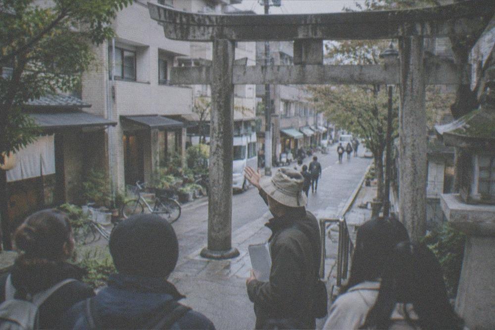 A guide speaking to a small group of visitors on a stone path beside a historic shrine gate