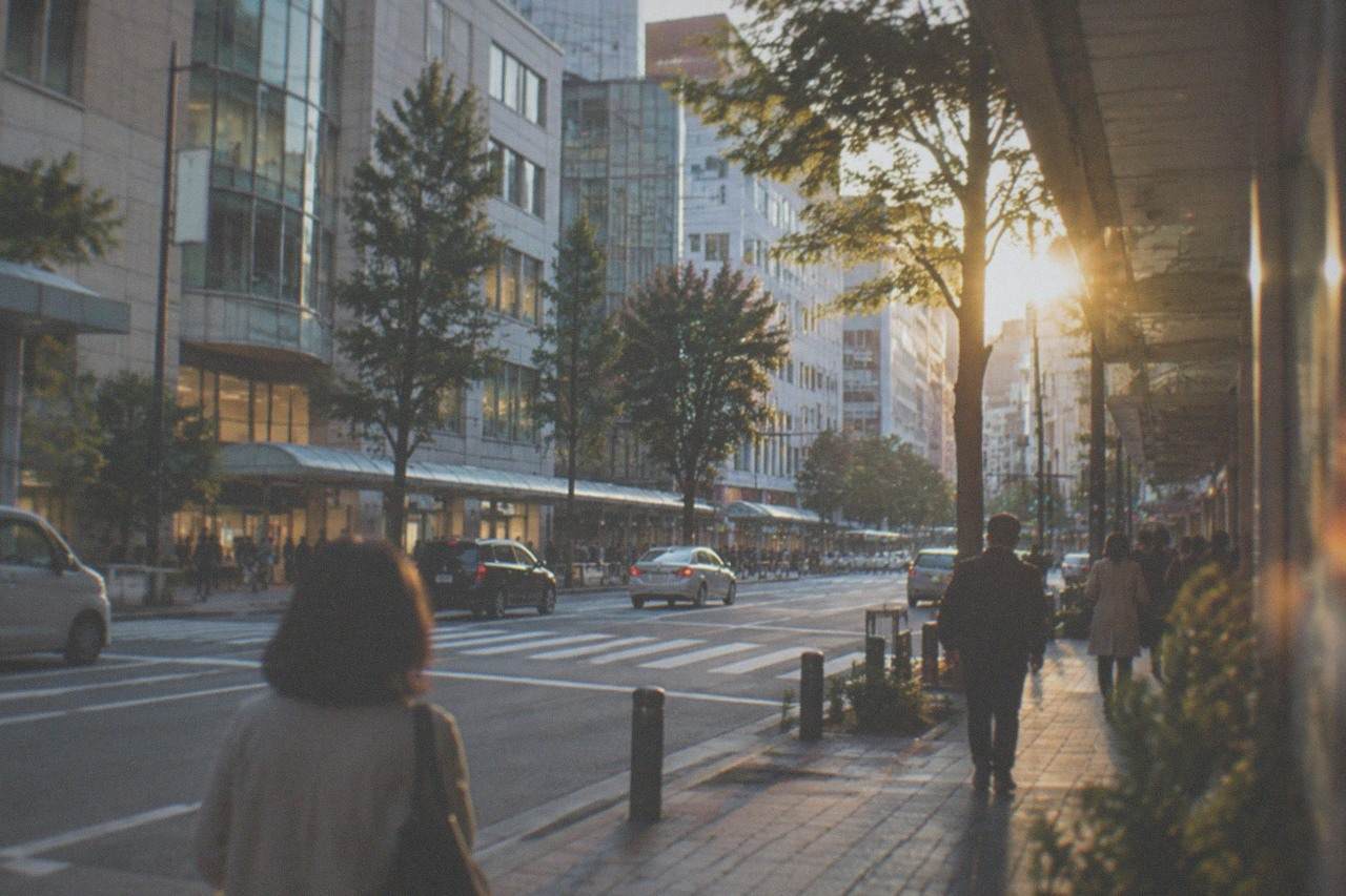 A wide street in central Fukuoka with illuminated shop signs and a subway station entrance in the evening
