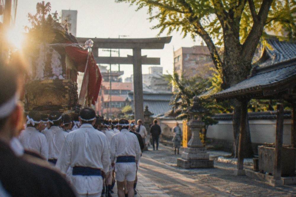 Team of men in traditional dress carrying a festival float through a crowded street at dawn