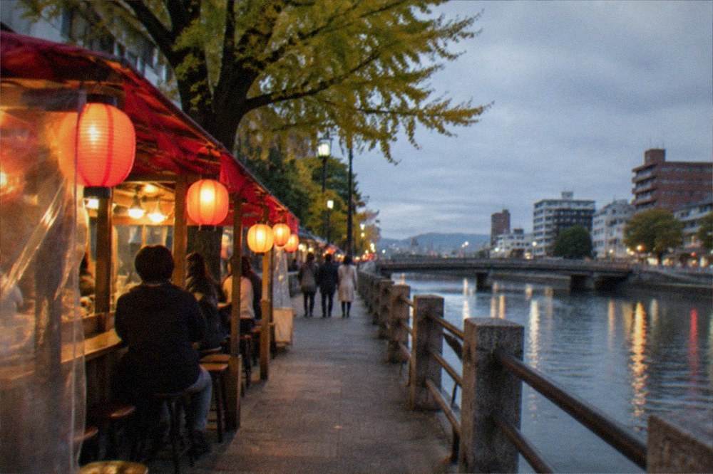 Food stall with lanterns glowing beside a river in the evening