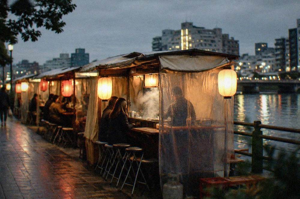 A row of glowing yatai food stalls lined up along a river at night