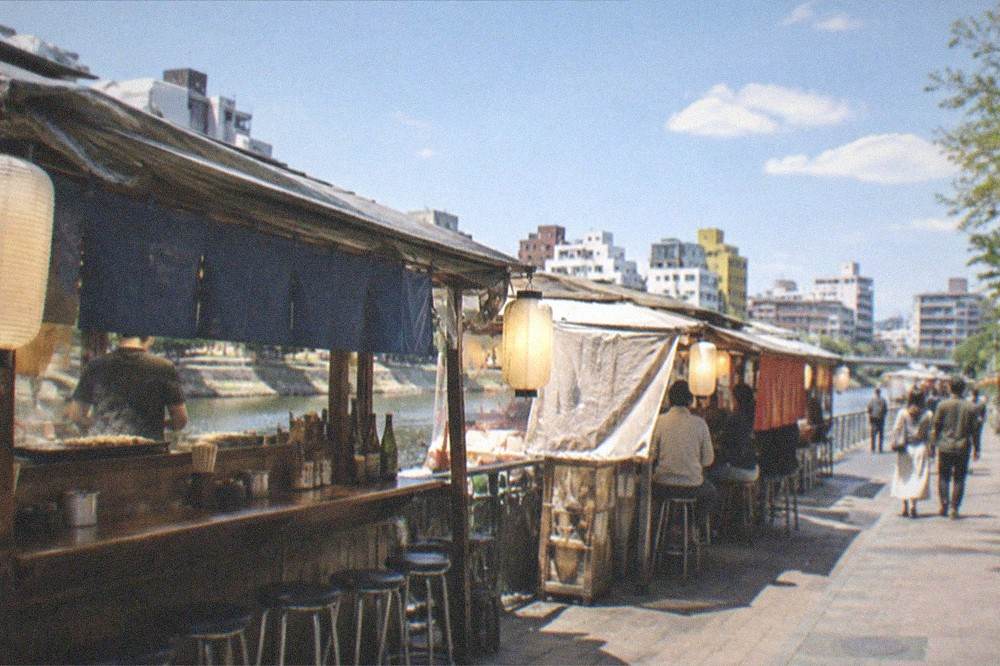 A small izakaya interior with lanterns, wooden counters and rows of sake bottles