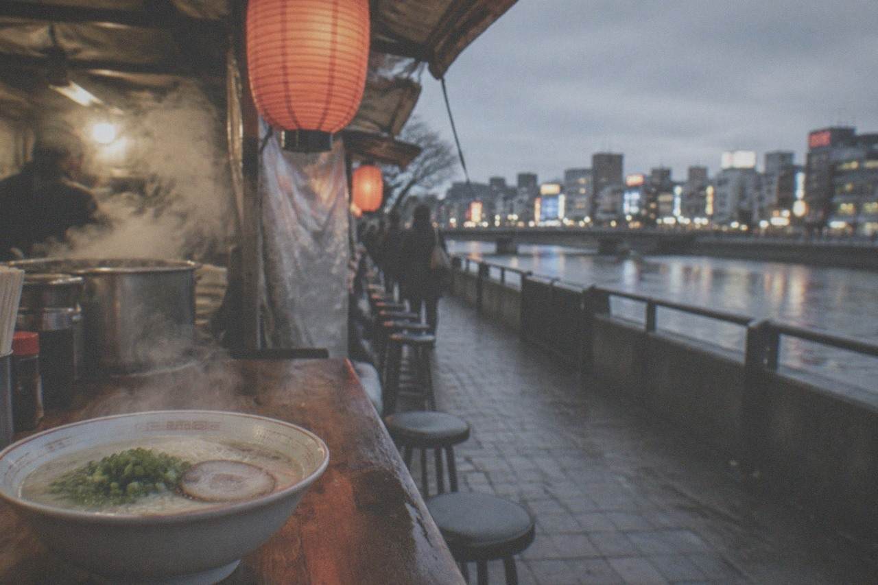 A steaming bowl of tonkotsu ramen with thin noodles, chashu pork and green onion on a wooden counter