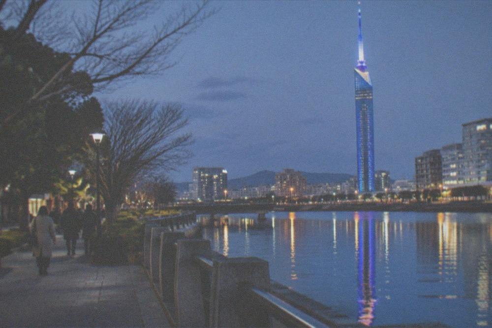 Night view of a illuminated tower reflected in still water along a waterfront promenade