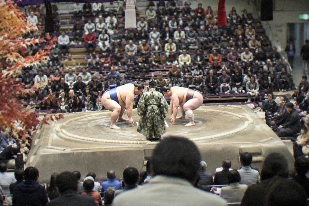 Sumo wrestlers competing on a clay ring inside a large indoor arena in Fukuoka