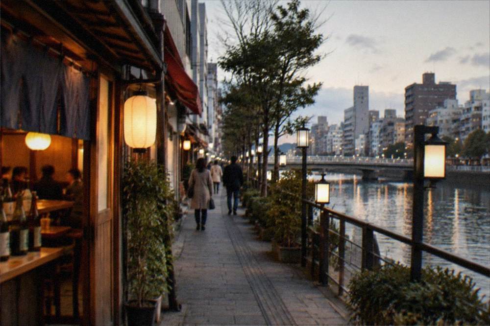 Warm lantern light inside a Nakasu izakaya at night with bottles of sake lined along a wooden counter