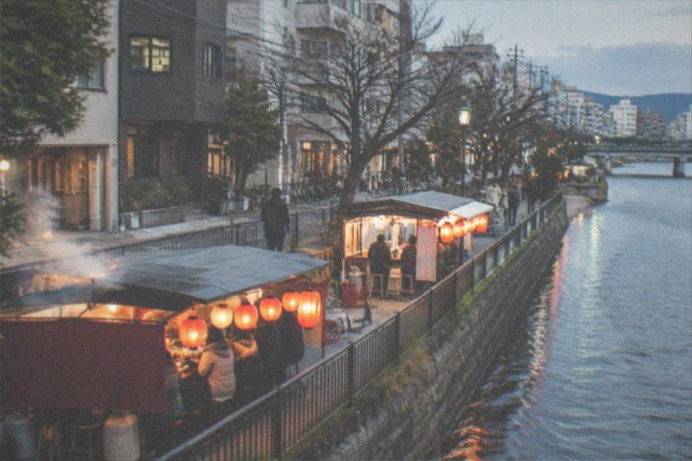 Steaming food stall with lanterns glowing beside a river at night