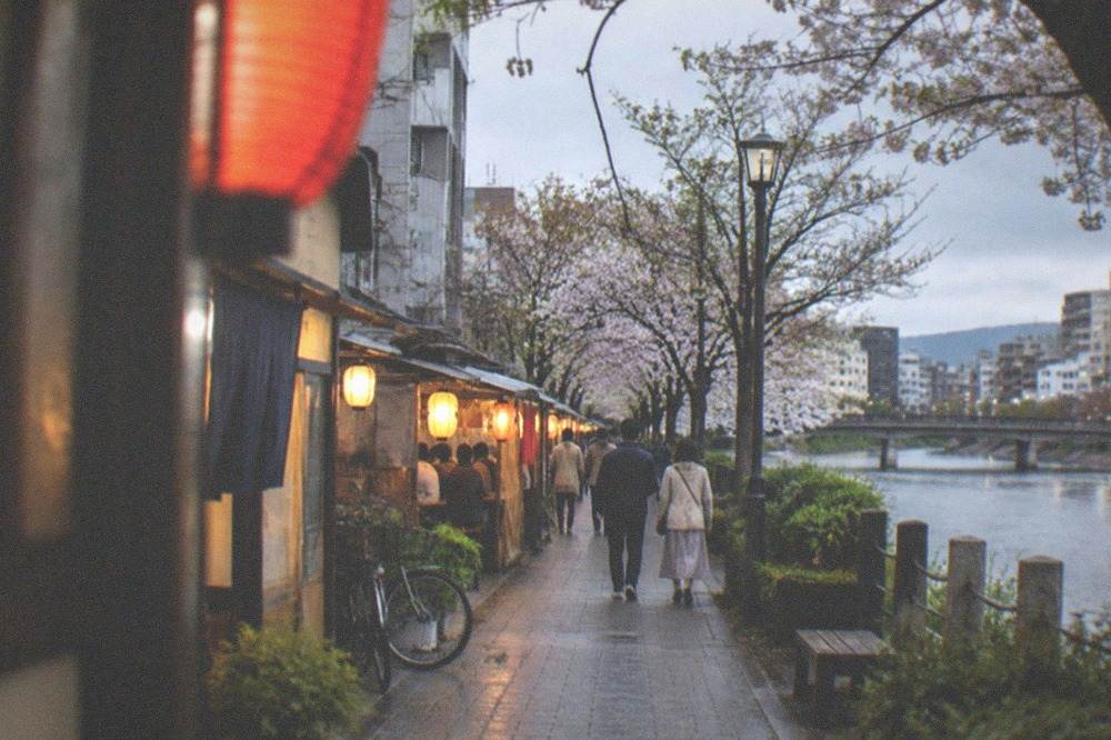 Wooden food stalls glowing with lanterns along a river at night