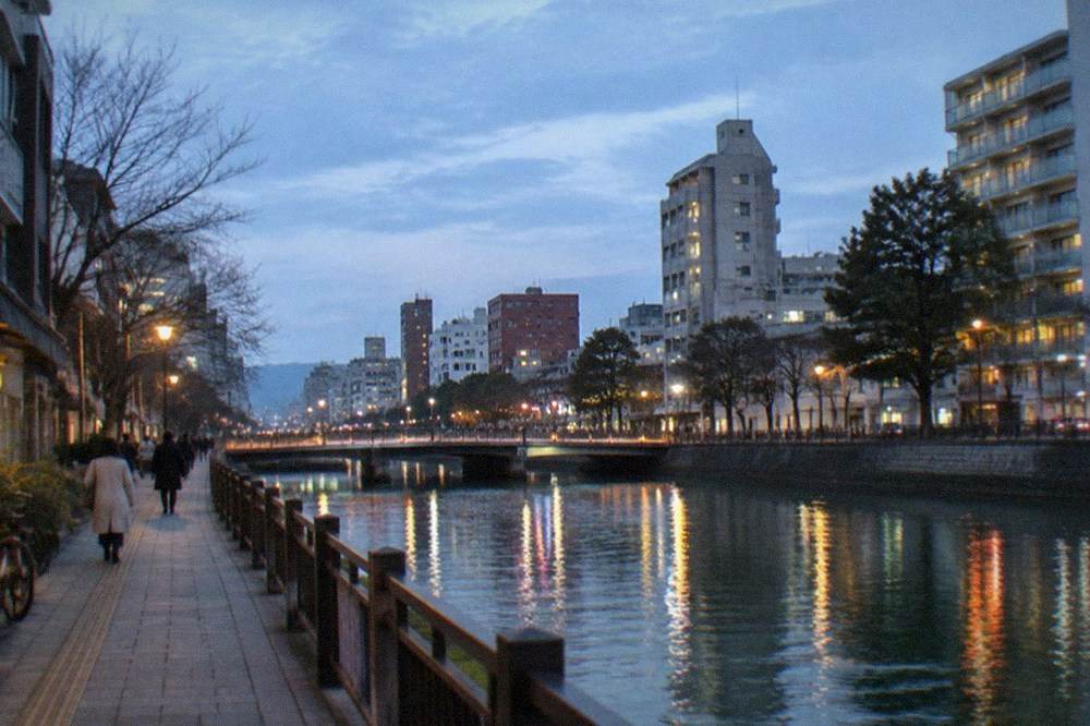 Evening illuminations reflecting on a canal in a Japanese city with tall buildings behind