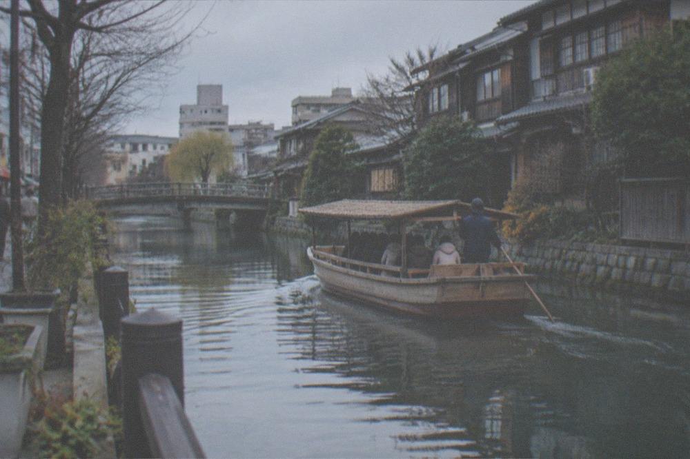 A wooden river boat gliding along a canal between old Japanese houses