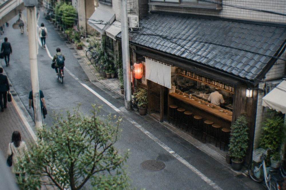 A small wooden izakaya counter with shelves of bottles and a single chef working behind it