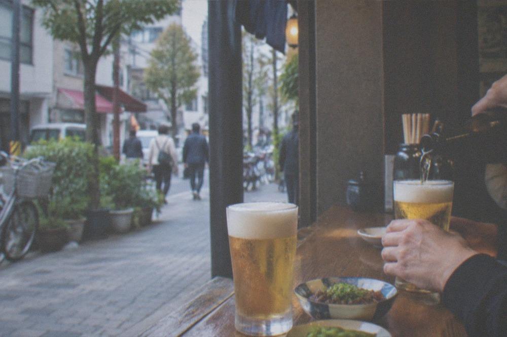 Two glasses of beer being poured at a wooden counter with small dishes of food