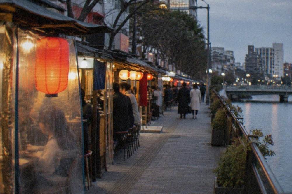 Evening lanterns glowing along a narrow street of food stalls beside a river