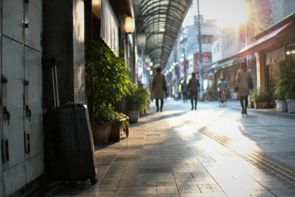 A quiet shopping arcade street in Hakata with a suitcase leaning against a wall near a locker bank