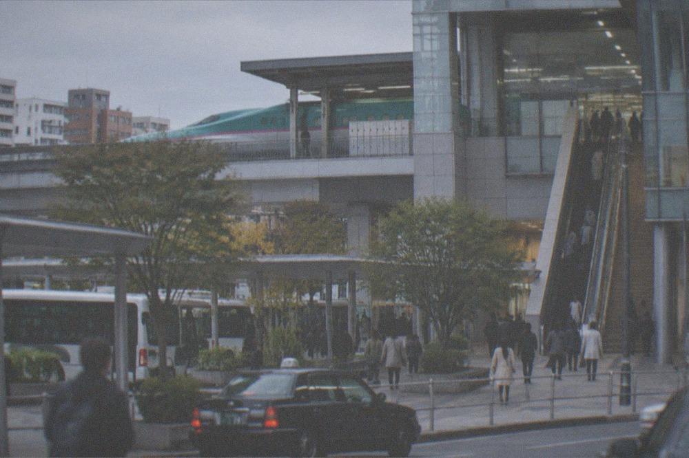 A shinkansen platform with a green train waiting and a locker bank visible at the top of the escalators