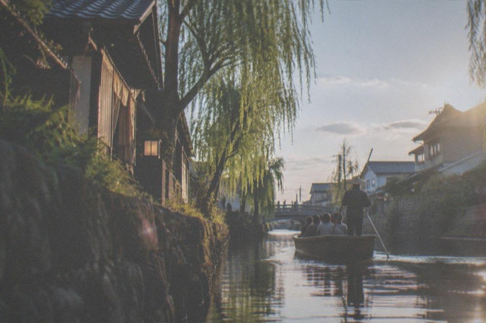 Small wooden punt boat gliding along a narrow canal between traditional houses