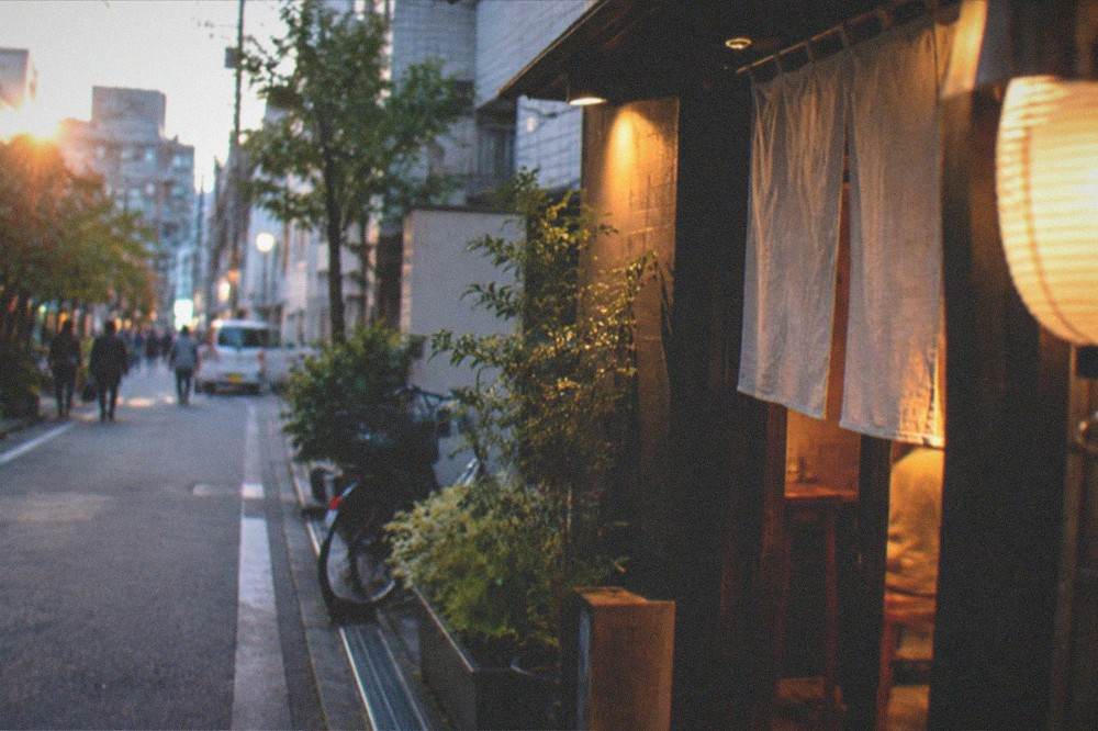 A quiet Fukuoka street corner at night with warm light spilling from a small restaurant doorway