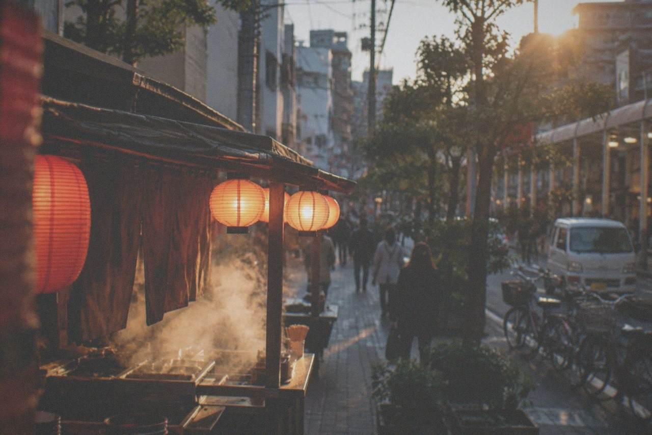 A lantern-lit street food stall at night with steam rising from a cooking counter