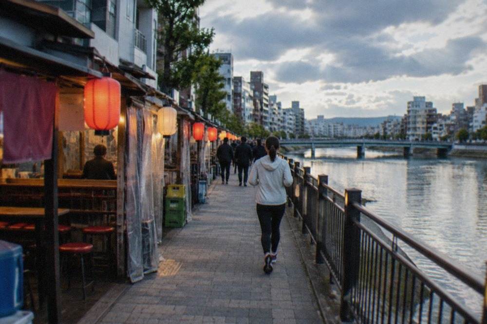 Illuminated food stalls and glowing signs along a riverside street at night in Fukuoka