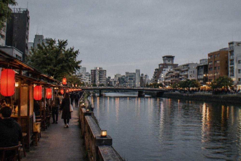 Red lanterns glowing outside wooden food stalls beside a dark river at night