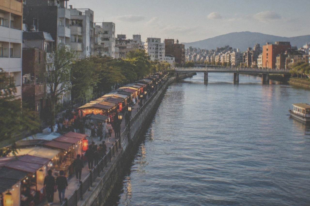 Illuminated food stalls and glowing signs along a riverside street at night in Fukuoka