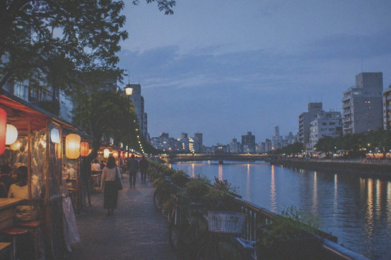 Food stalls with lanterns glowing along a riverside street in the evening