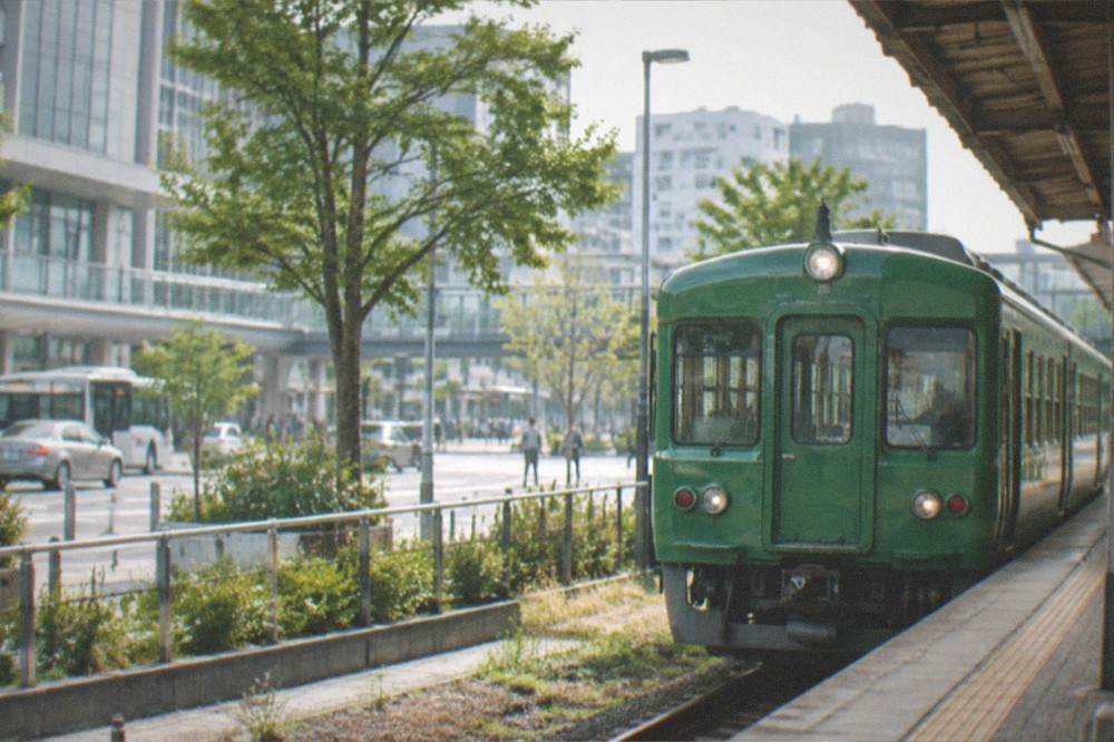 A green sightseeing train waiting at a small rural station platform