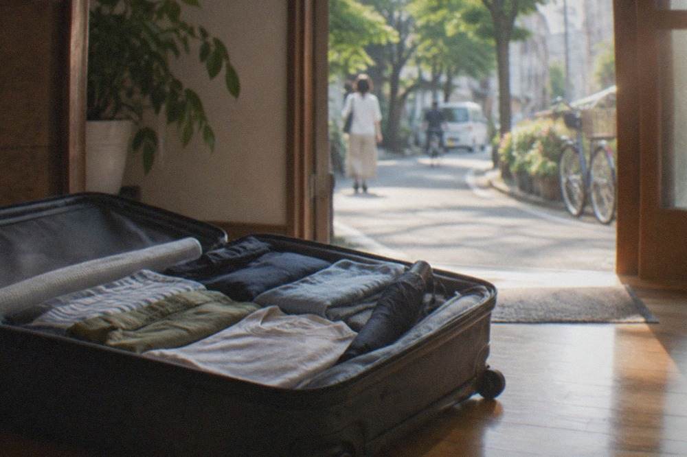 A packed suitcase open on a wooden floor with folded summer clothes and a compact umbrella