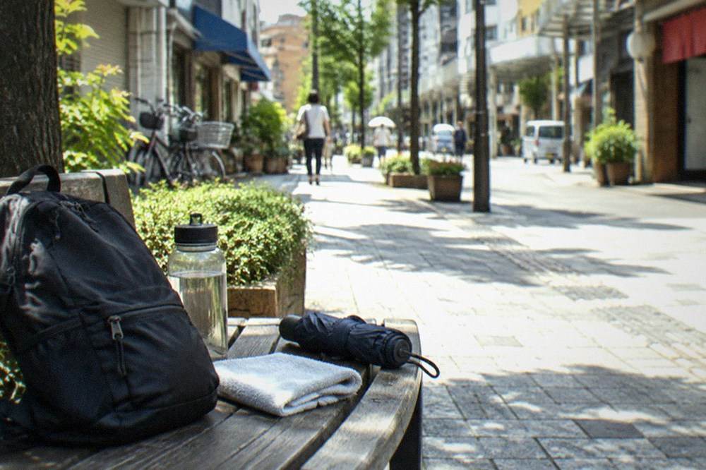 A small day pack on a bench beside a water bottle, a folded towel and a compact umbrella