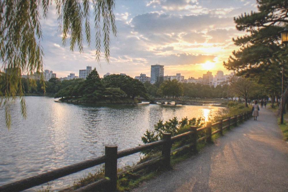 A park pathway at golden hour with distant city office towers