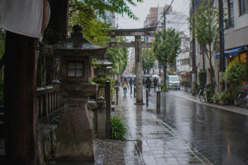Rain-wet stone lanterns and pavement along a narrow shrine approach in Fukuoka