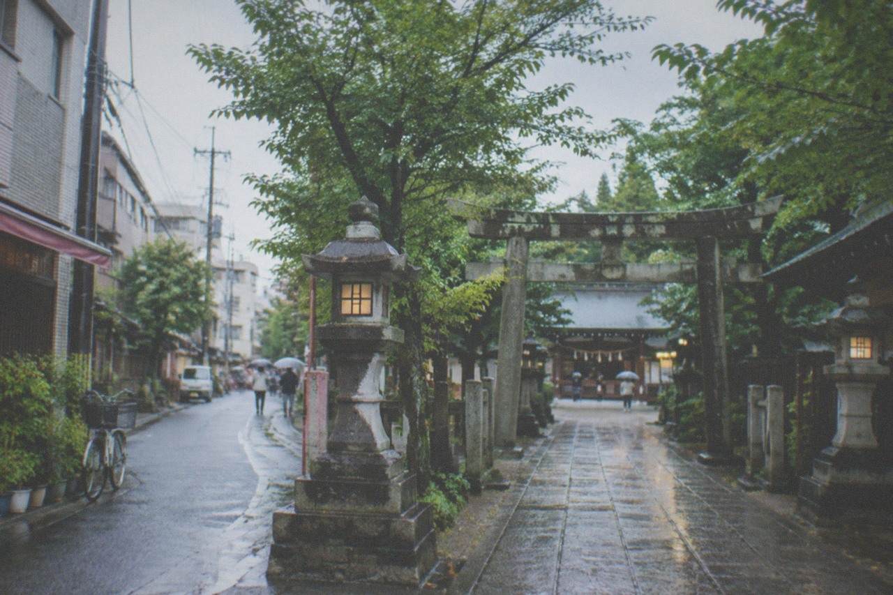 Rain-wet stone lanterns and pavement along a narrow shrine approach in Fukuoka