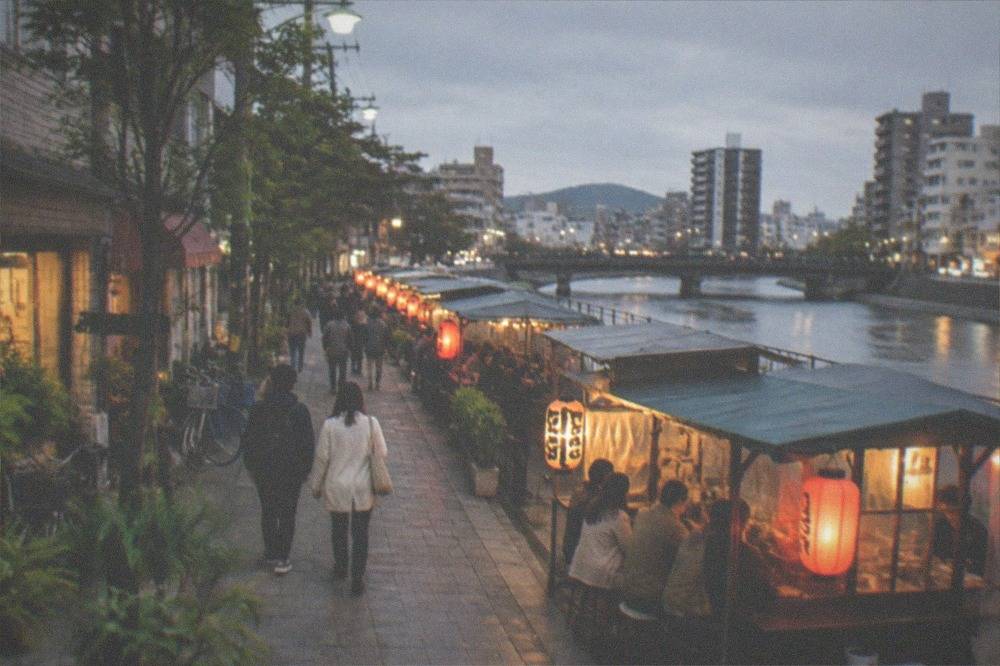 Lantern-lit food stalls lining a riverside street in the evening