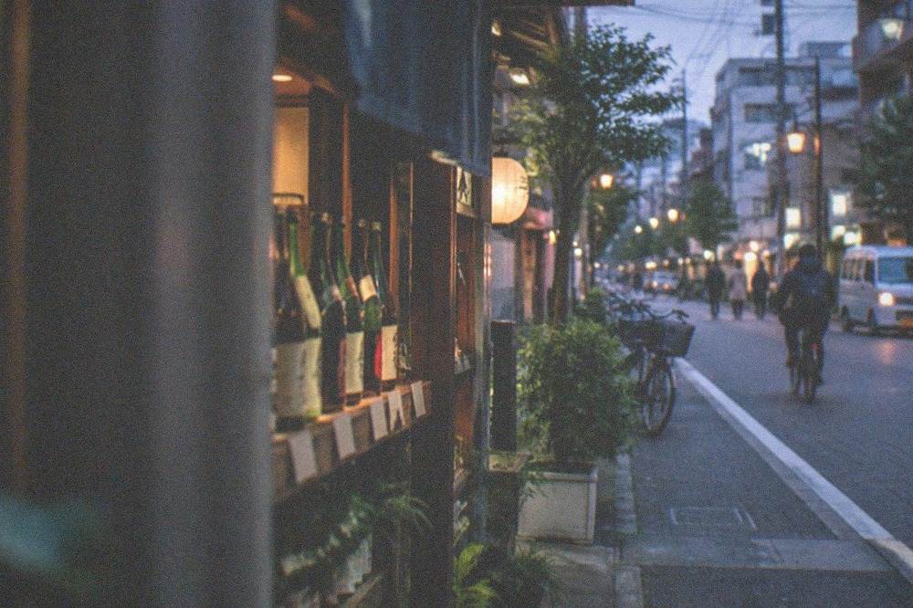 A row of sake bottles with handwritten price tags on the shelf of a small shop