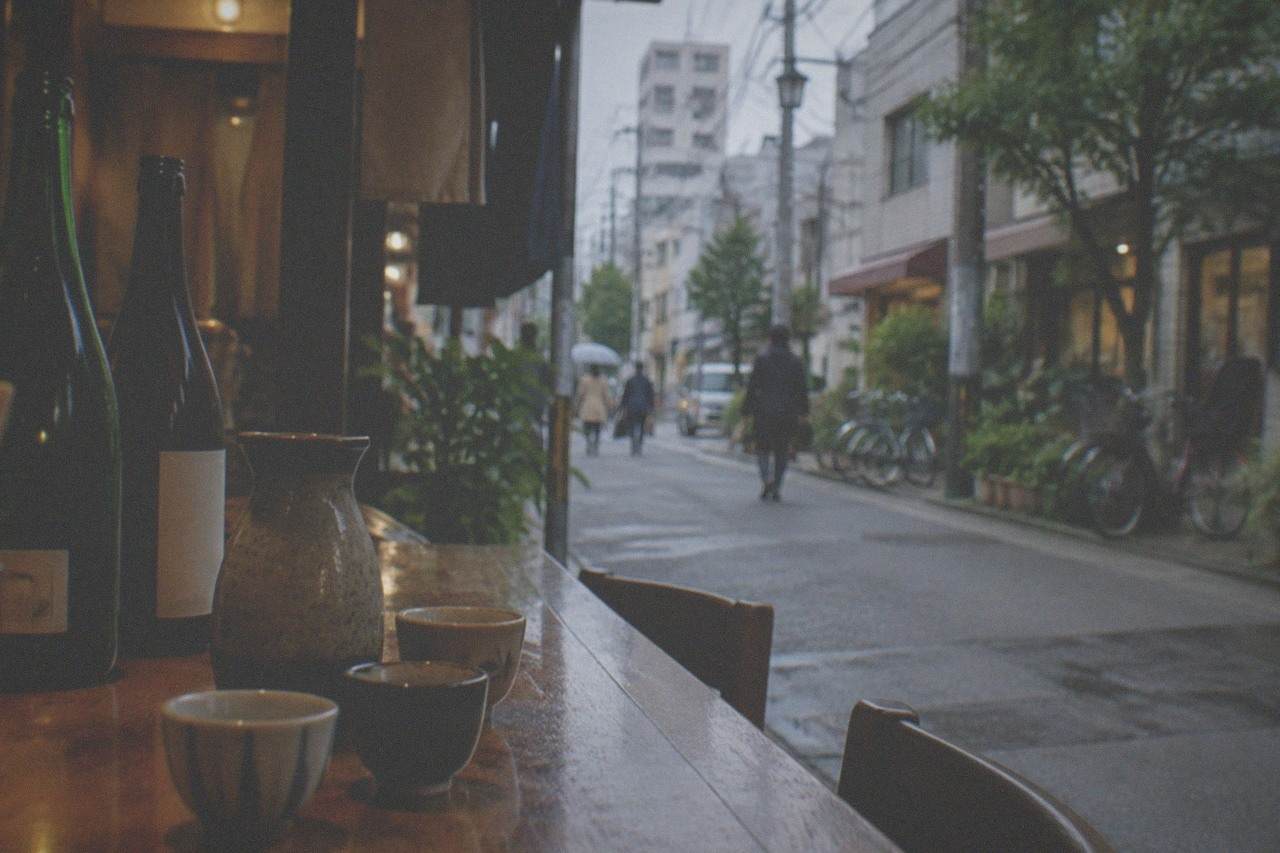 Sake bottles and small ceramic cups arranged on a wooden bar counter in warm light