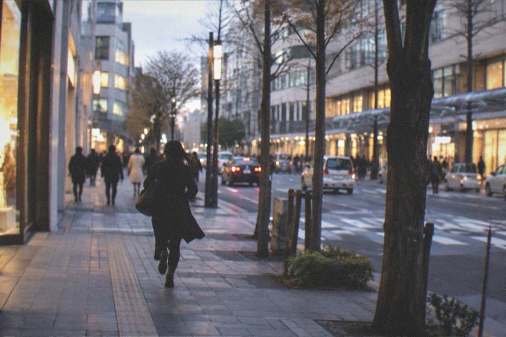 Evening city street with illuminated shopfronts, neon signs and shoppers walking between lit entrances