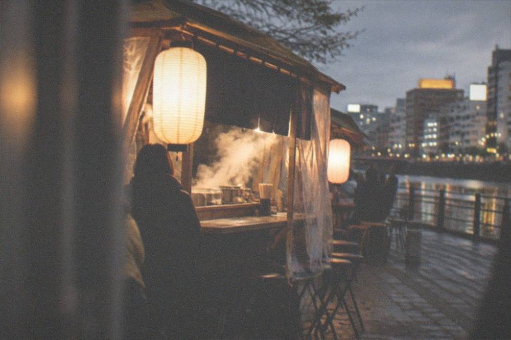 A glowing yatai food stall at night with steam rising from its counter