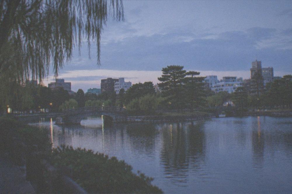 A calm pond in Ohori Park with a stone bridge and city buildings behind