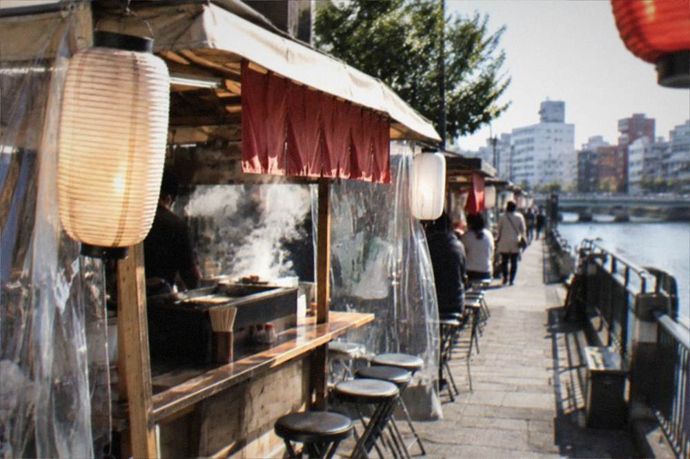 A handwritten price menu on a wooden board clipped to a food stall