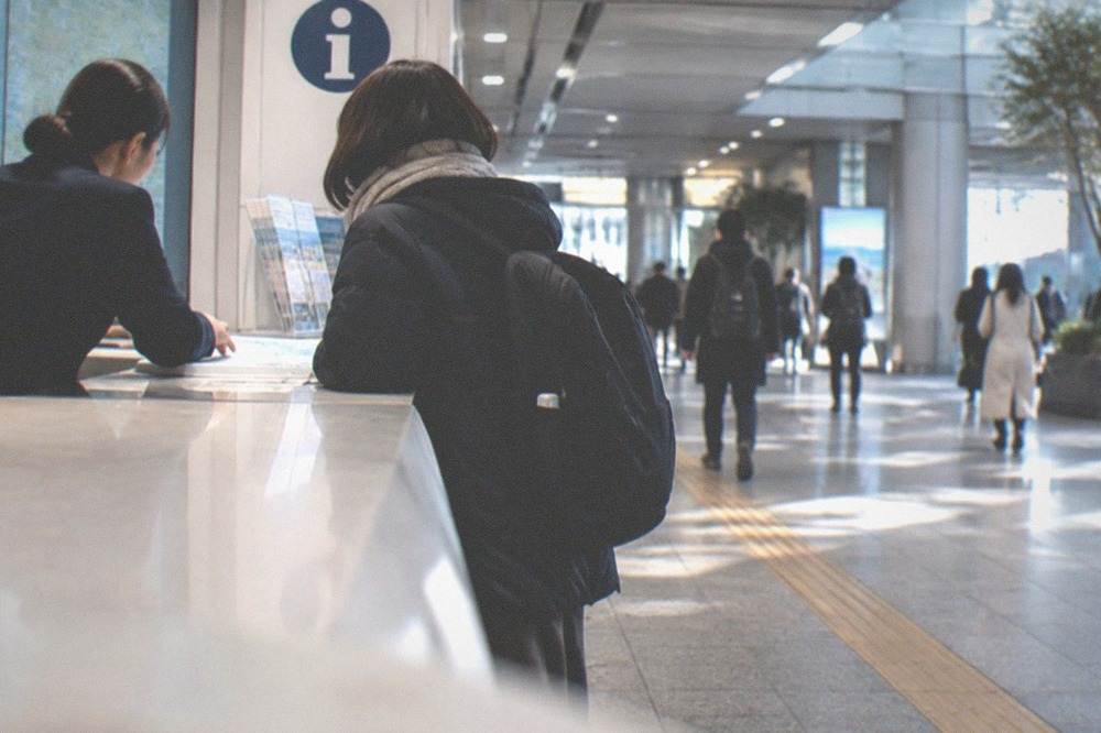 A tourist information counter in a Fukuoka subway station with staff assisting a traveller