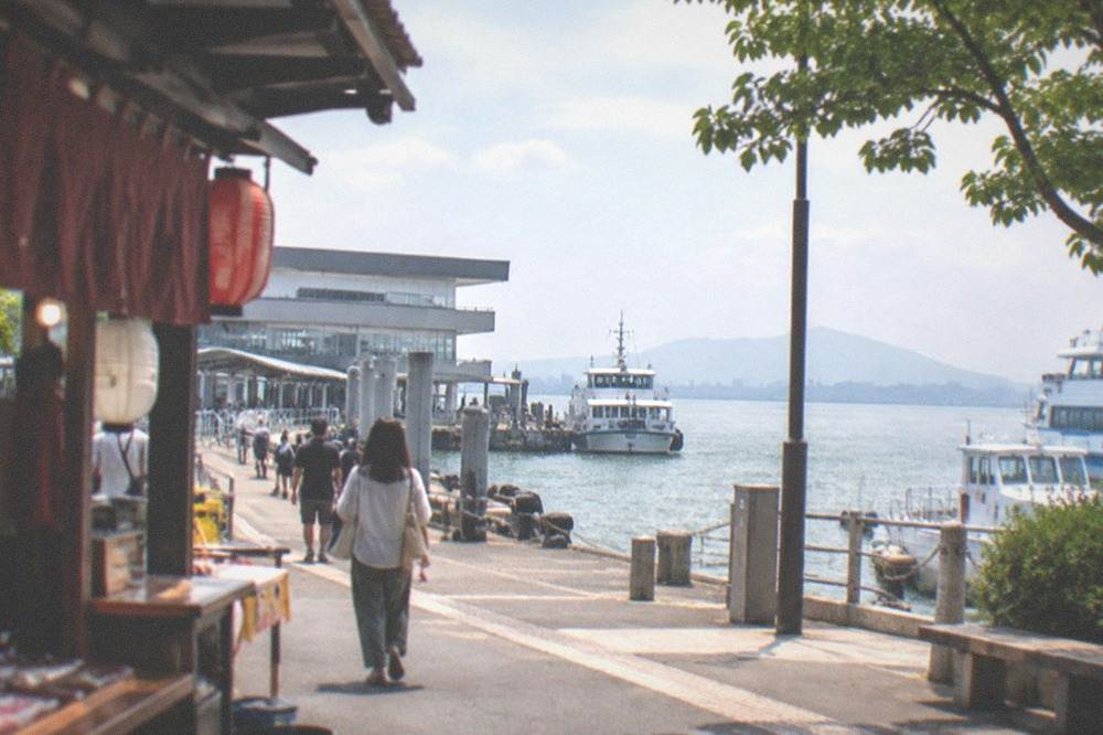 Food stalls with lanterns and posted menus lined along a river embankment at dusk
