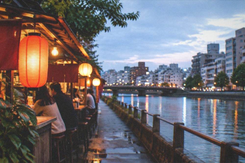 A glowing food stall beside a river at night with lanterns and counter seating